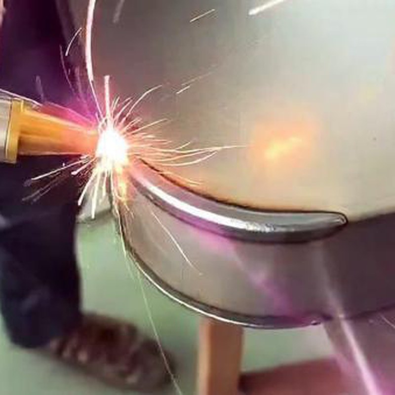 Handheld laser welding tip joining a curved metal seam